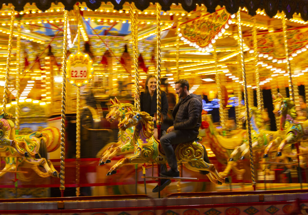 woman and man sit on a merry go round at night, laughing together