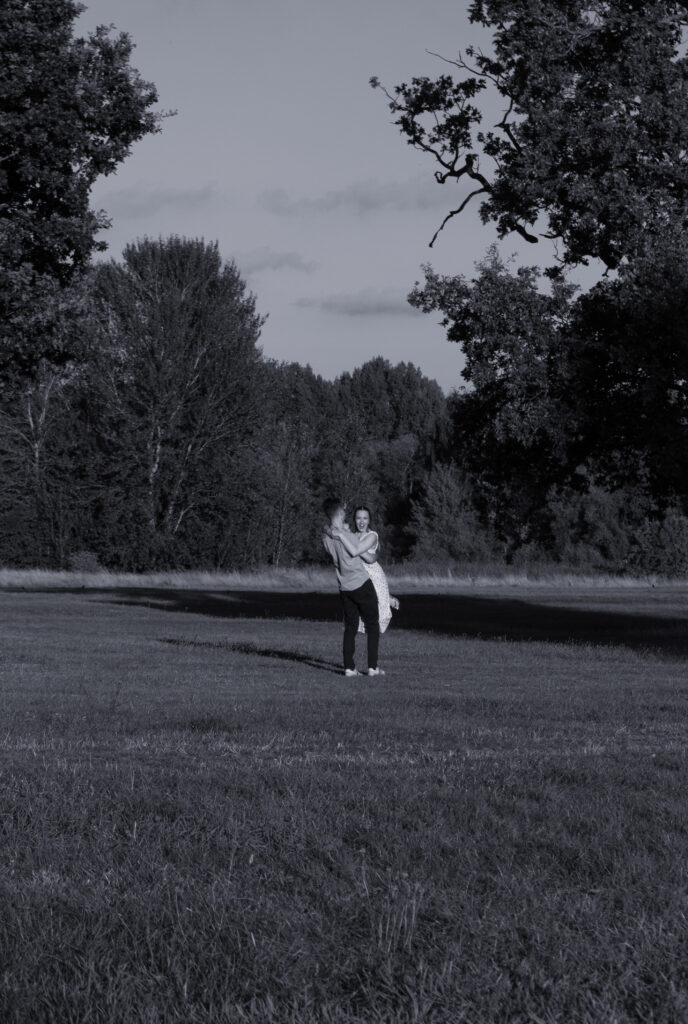 Elegant engagement photo of a romantic couple dancing together outdoors at sunset in London meadow, at golden hour. 