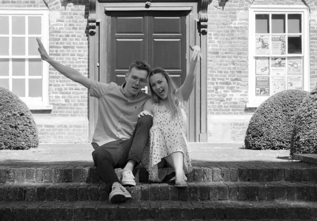 Fun and quirky engagement photo of a couple sitting on steps and making playful gestures. Perfect pre-wedding photography session for couples.