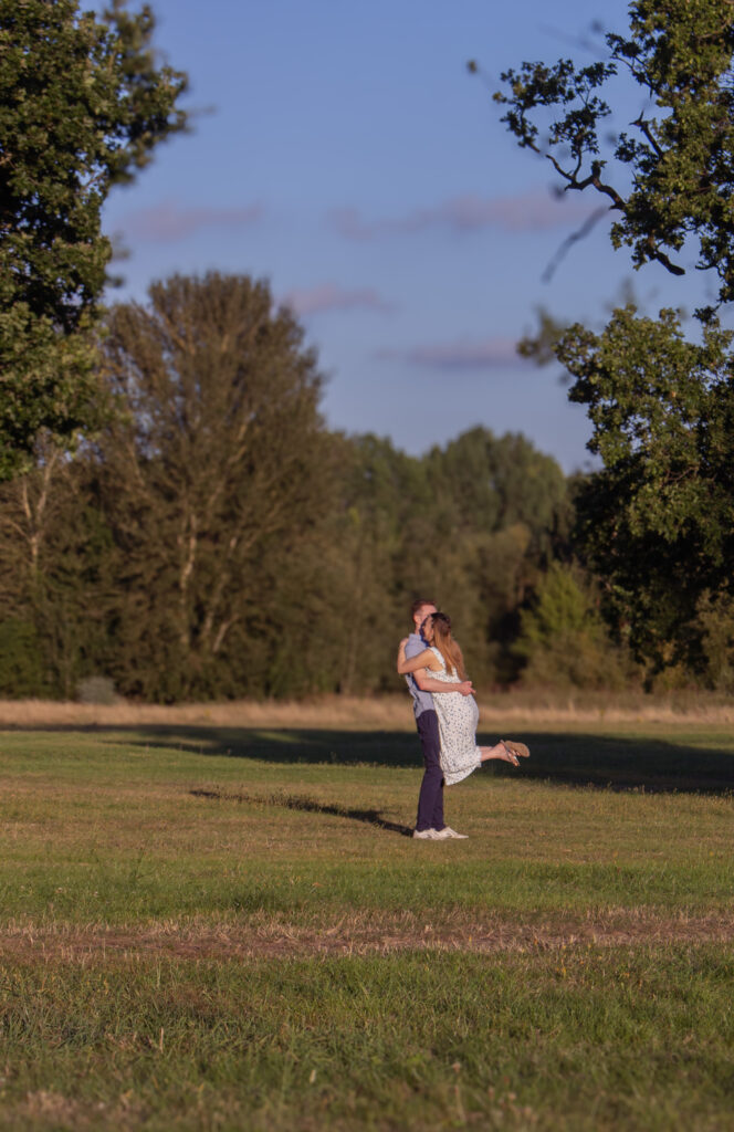 Elegant engagement photo of a romantic couple dancing together outdoors at sunset in London countryside, at golden hour. 